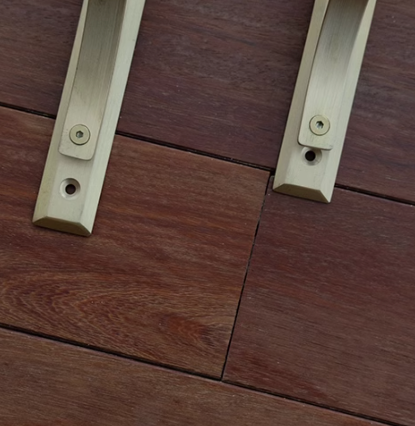 Two brushed brass shelf brackets on a dark wood surface.